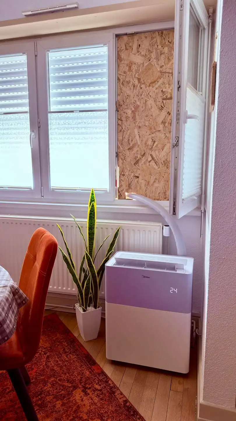 Le PortaSplit posé dans une salle à manger contre le radiateur, tuyau de liaison remontant vers la fenêtre entrouverte